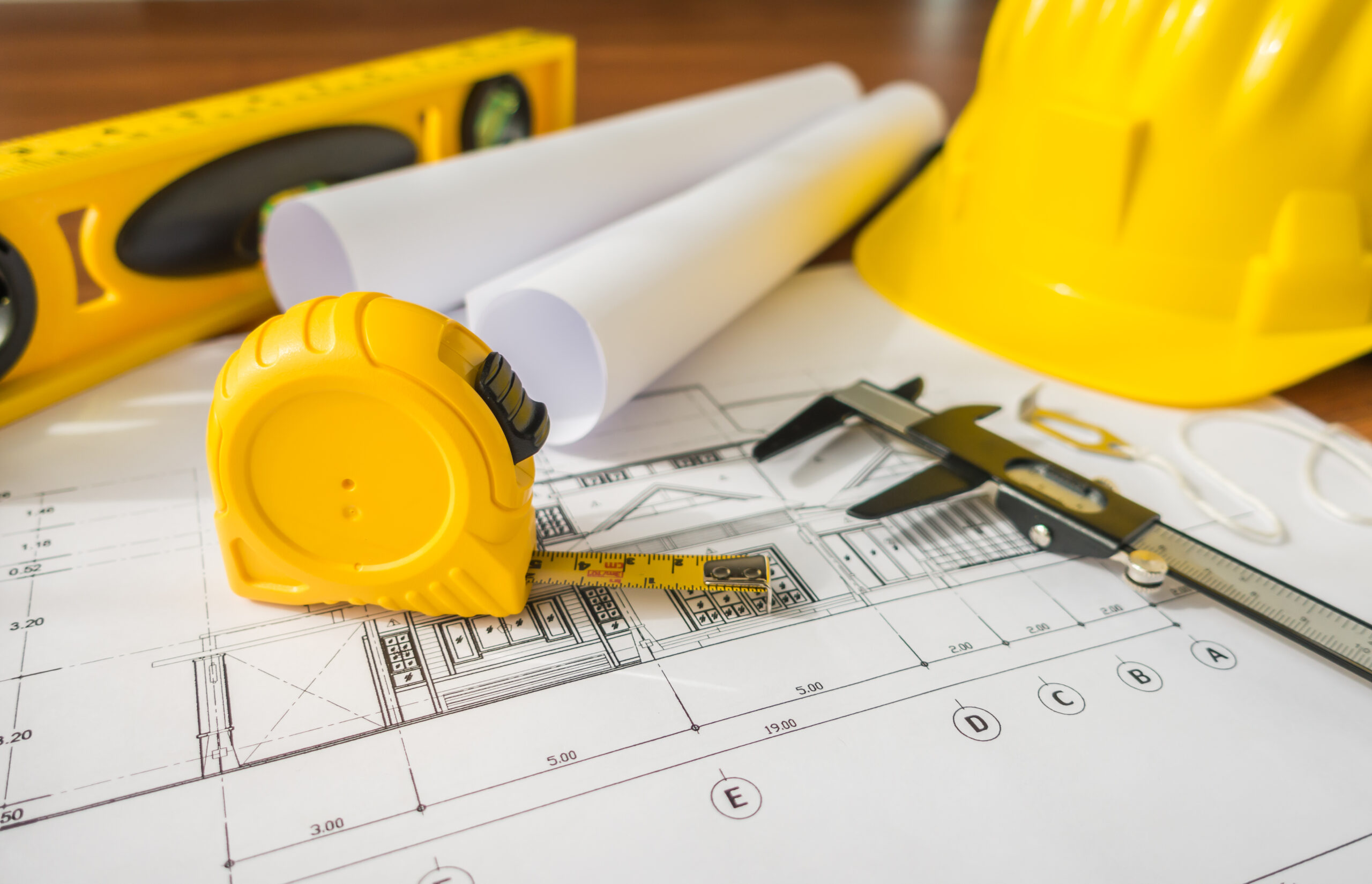 Construction plans with yellow helmet and drawing tools on blueprints